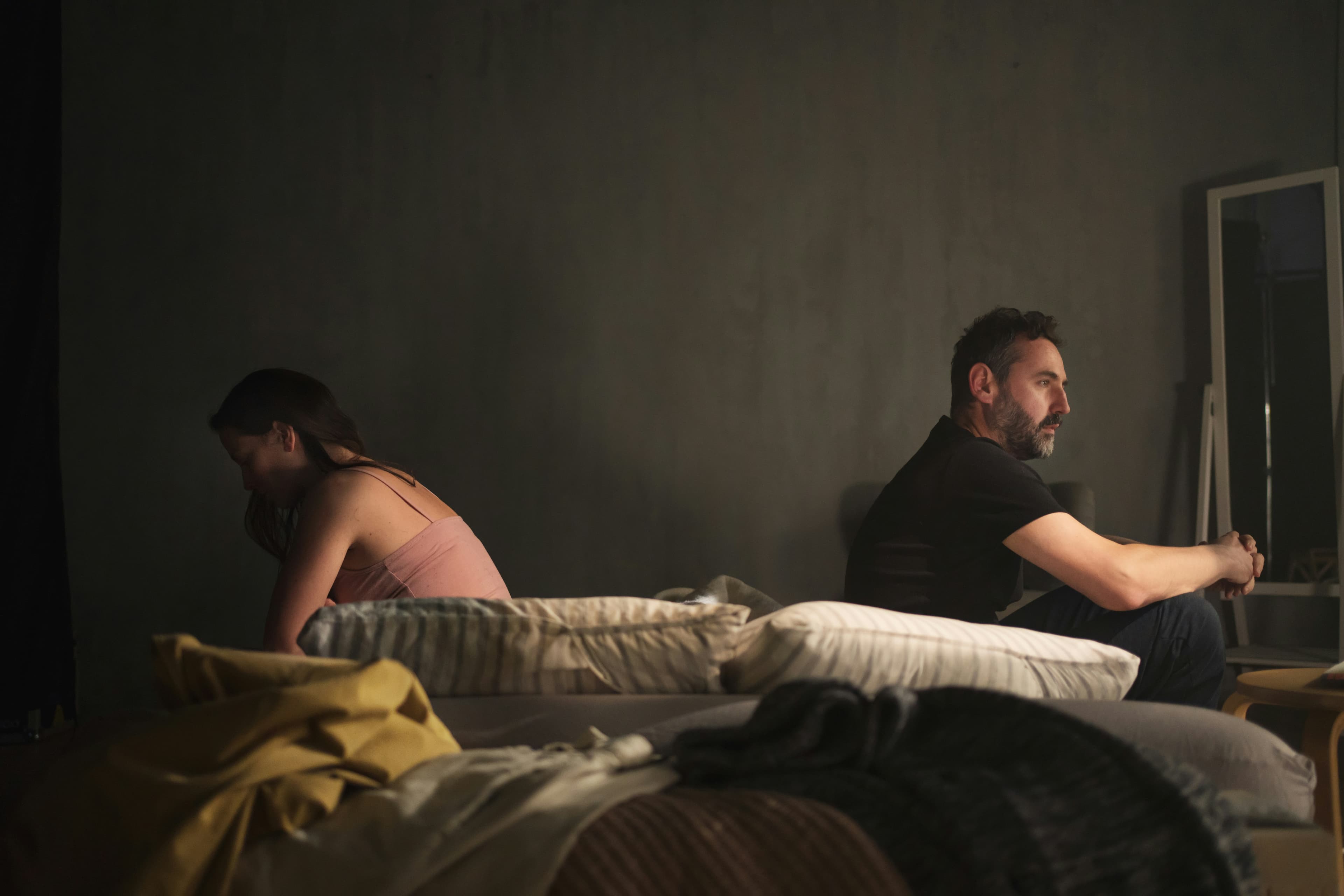 Couple sitting apart on opposite sides of the bed, illustrating the emotional distance caused by compulsive pornography use