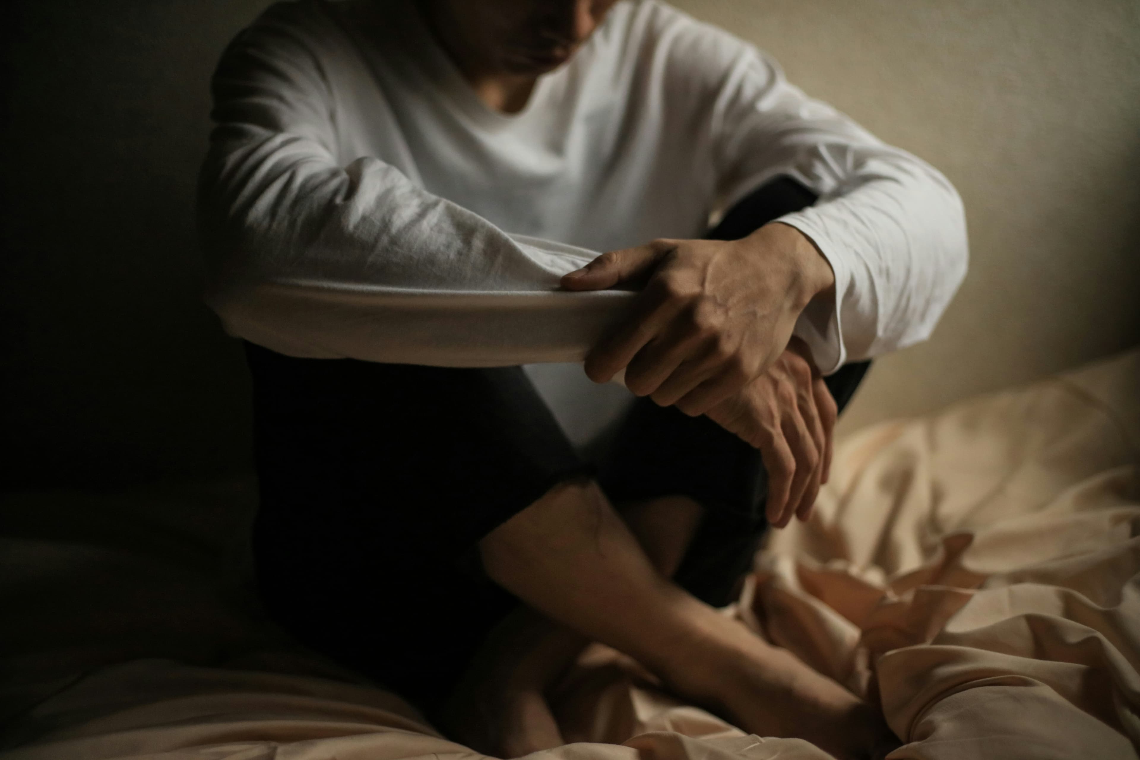 Man sitting alone on a bed in a dark room, reflecting the isolation of compulsive pornography use